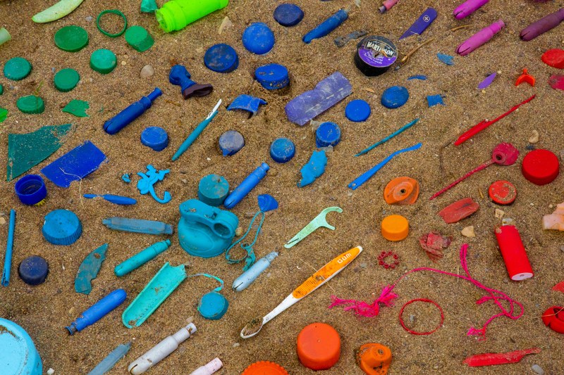 Picture of plastic marine litter placed in colour order (green, blue, orange, red) in the sand.