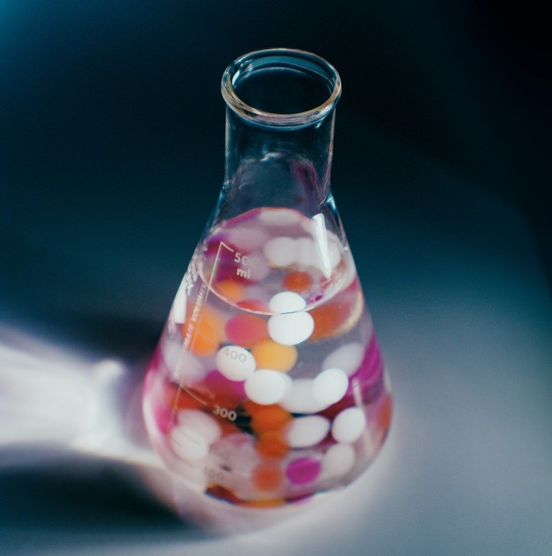 Picture of a 500ml glass flask with a transparent liquid and reflections of coloured circles inside.