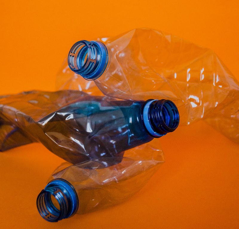 Picture of three empty and slightly crushed transparent water bottles with a blue rim but no cap on an orange background.