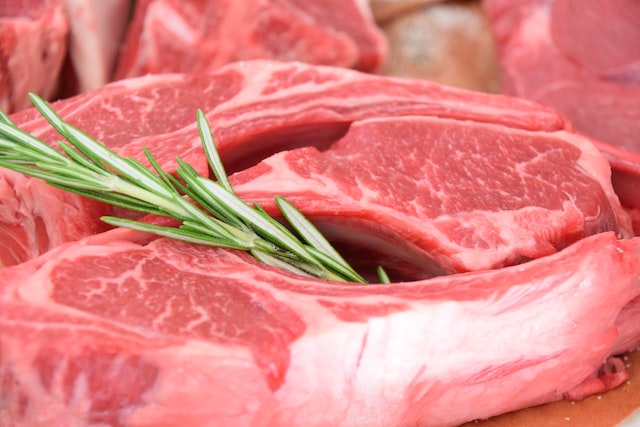 Picture of a close-up of a raw bone steak with a rosemary leaf placed in the centre of it.