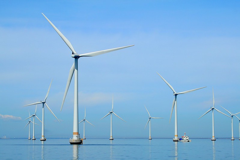 Picture of ten wind energy windmills in a clear lake with a small boat visible on the bottom right and in a clear blue-sky setting.
