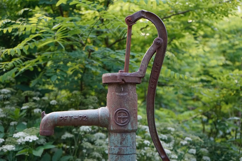 Image of a rusted brass water well-hand vintage pump in a green forest background setting.